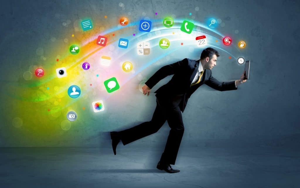A man in a suit runs while holding a tablet, with colorful app icons and digital symbols swirling out from the device against a gray background, symbolizing technology and connectivity.