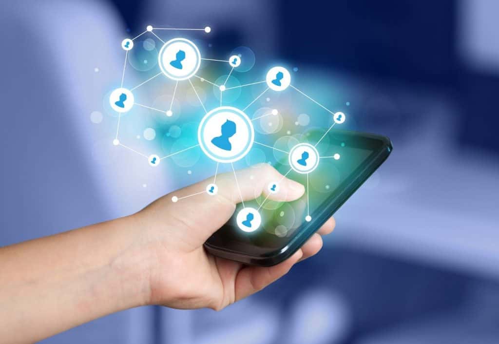 A hand holds a smartphone with a digital overlay of connected user profile icons, symbolizing social networking or digital communication, against a blurry background.